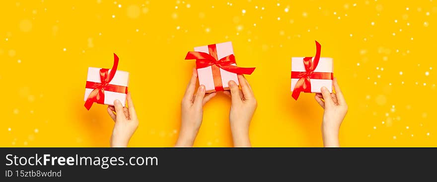 Merry Christmas and 2022 Happy New Year card. Woman hands hold surprise boxes with red bow on yellow background, top
