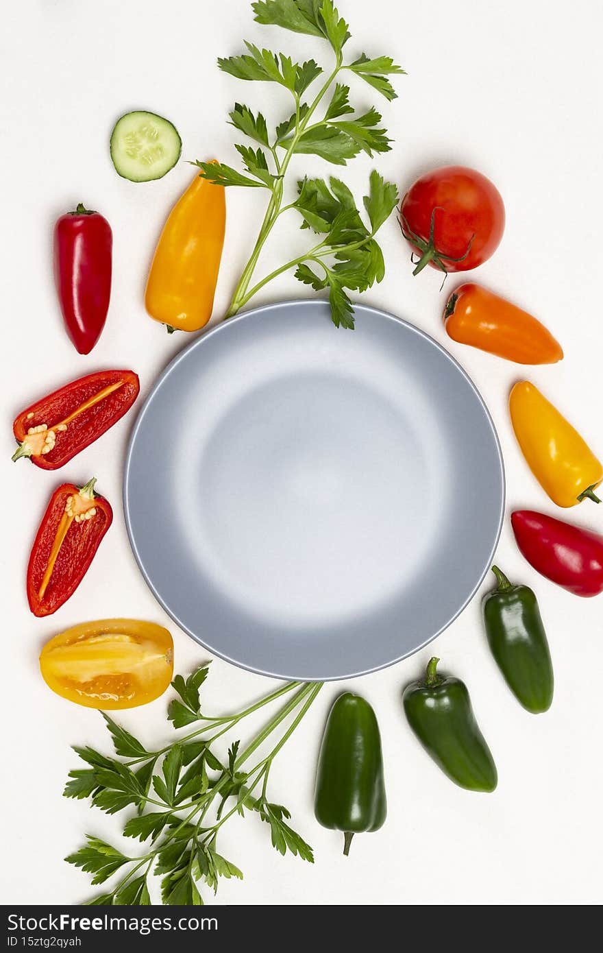 Empty gray plate. Sprigs of parsley, green and red peppers, tomatoes on table