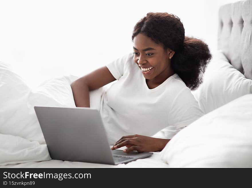 Cheerful african american lady surfing on Internet in bed