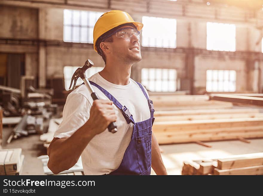 Handsome young man construction worker looking up and smiling while holding hammer tool. Handsome young man construction worker looking up and smiling while holding hammer tool
