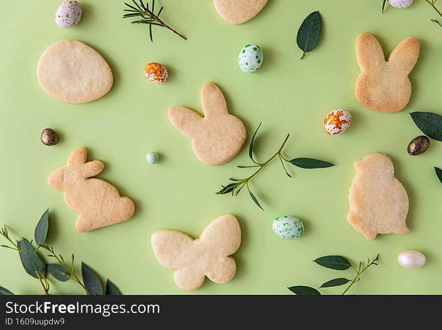 Easter cookies, candies shaped eggs, eucalyptus, flowers and quail eggs on green pastel background. Happy Easter concept. Pattern