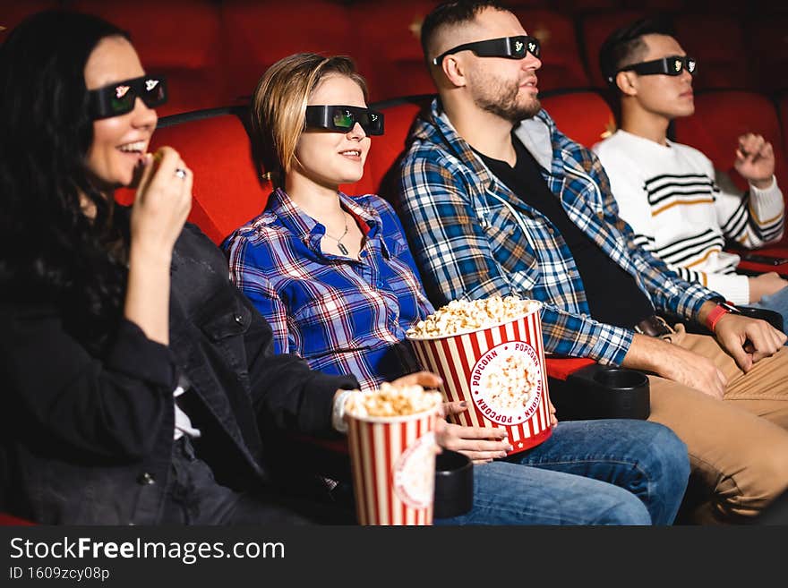 Friends are watching a movie in the cinema. People sit in the armchairs of the cinema and look at the screen with special glasses for 3D.