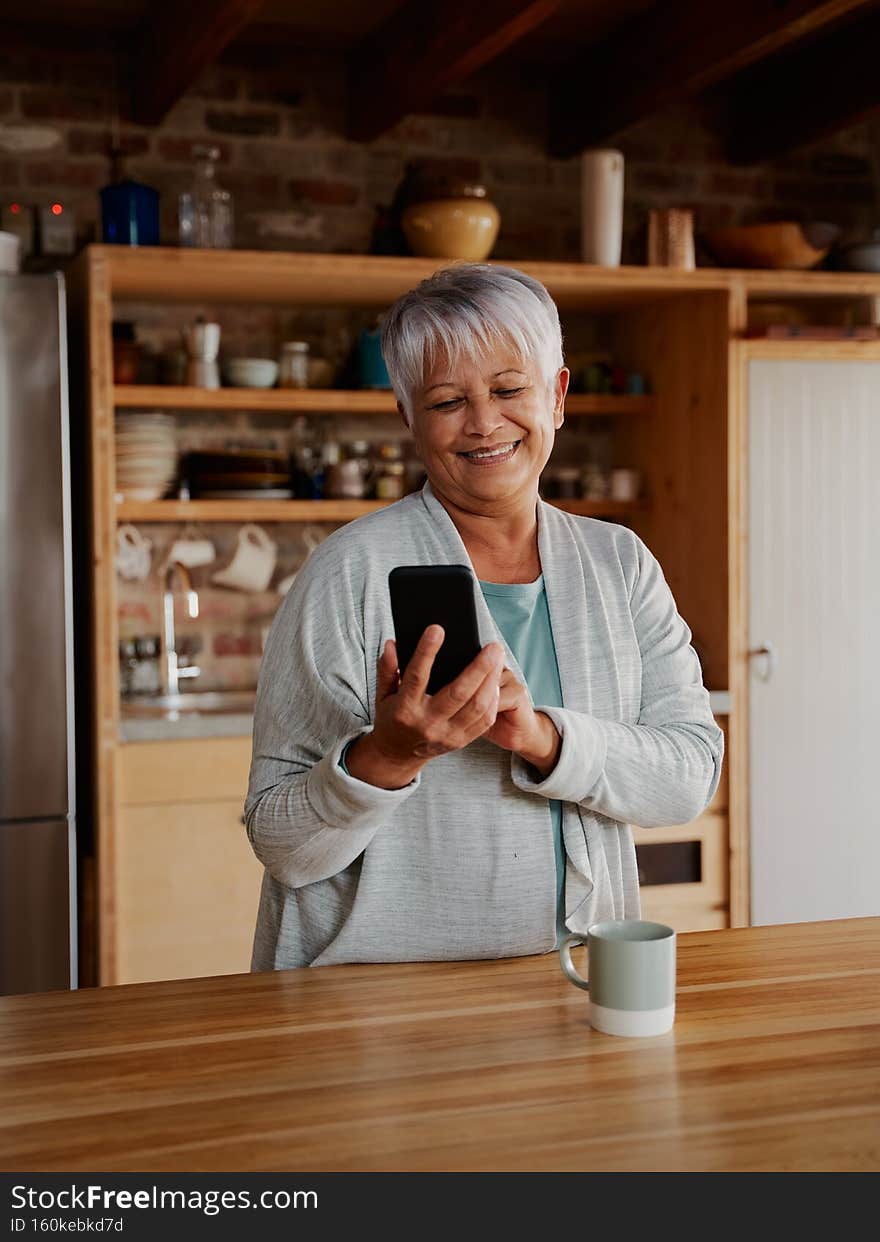 Portrait orientation of happy multi-cultural elderly female typing a message on smartphone while standing in modern