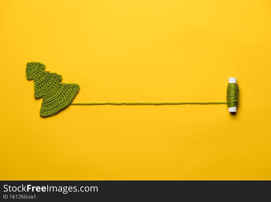 Knitted Christmas tree - a symbol of the New Year, with a spool of thread, with a place for text, on a yellow background