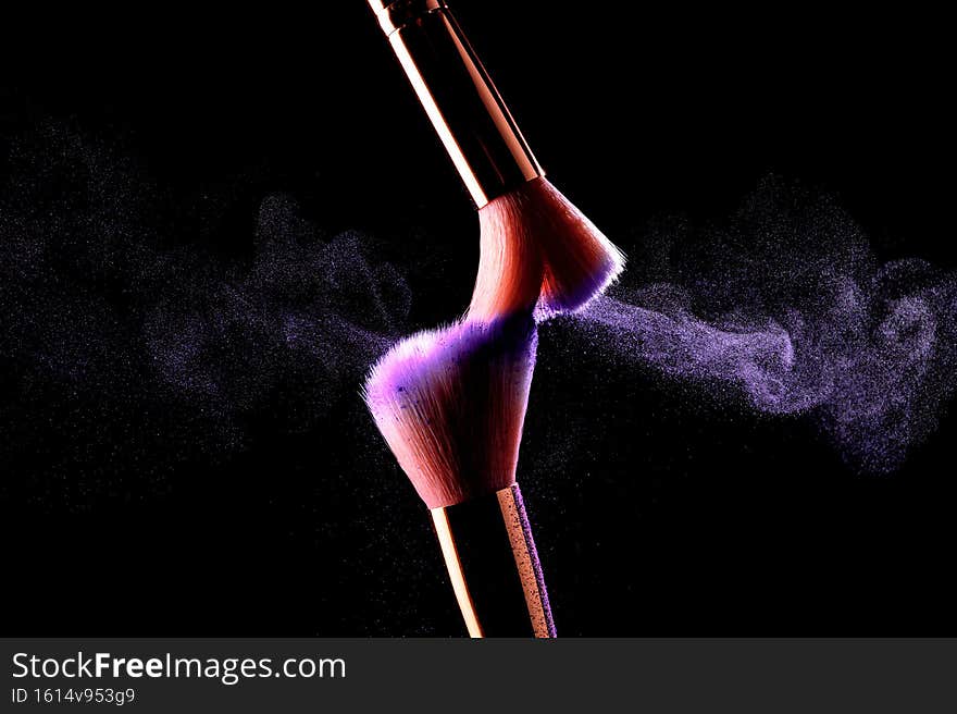 Make-up brushes with cosmetic powder explosion on black background.