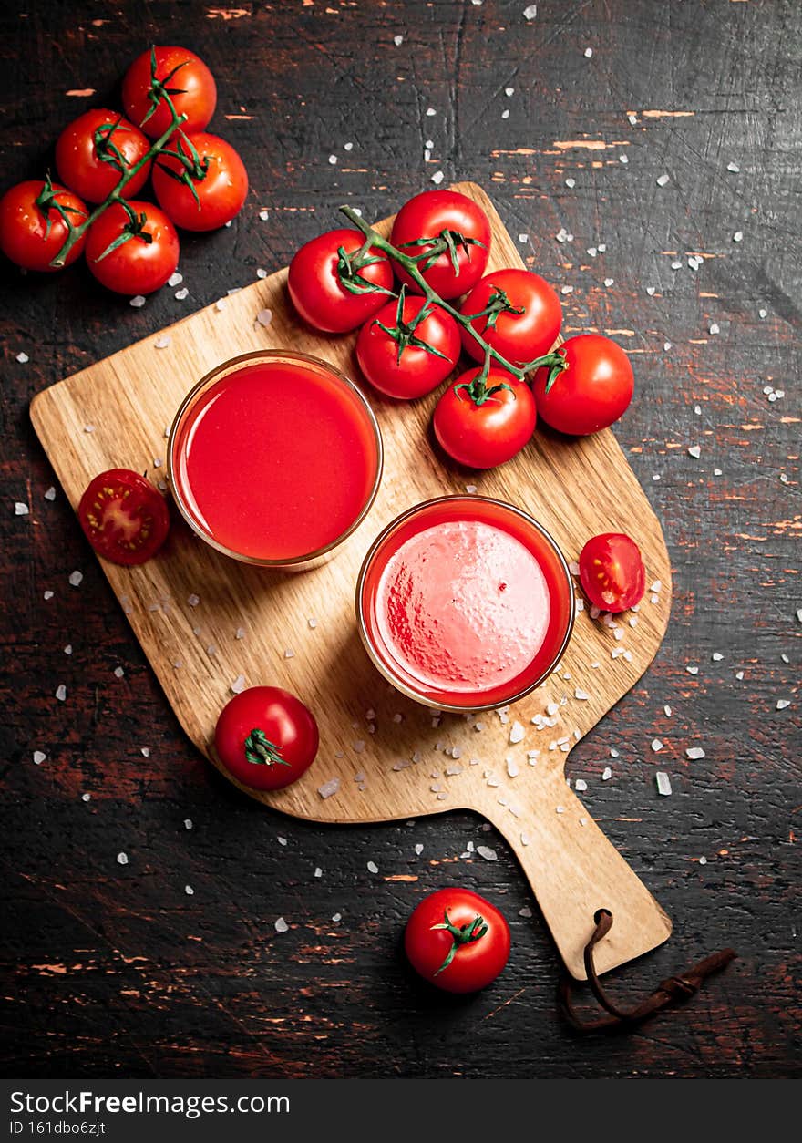 Tomato juice in glasses on a wooden cutting board.