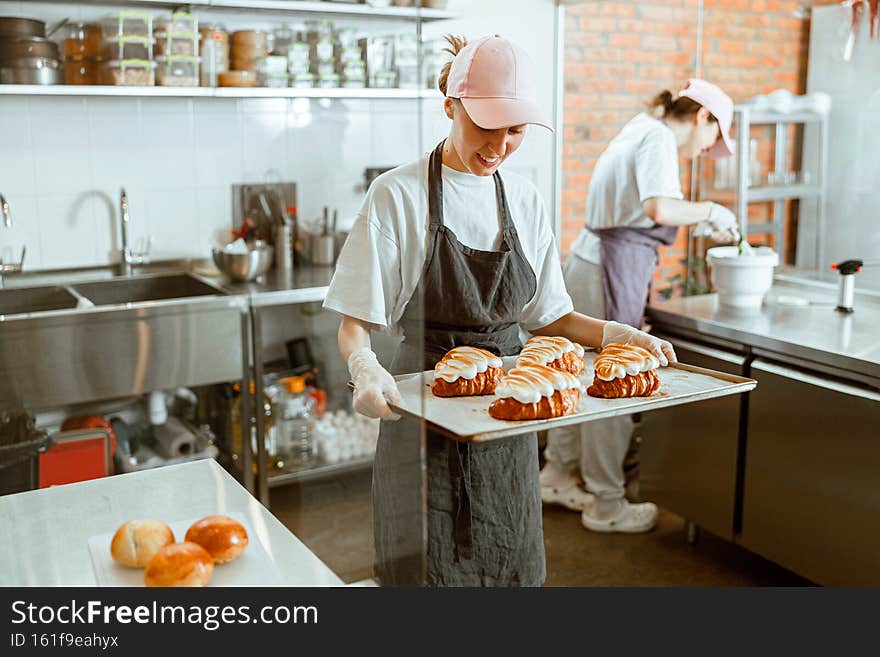 Smiling woman holds tray with delicious croissants decorated with burnt cream in craft bakery