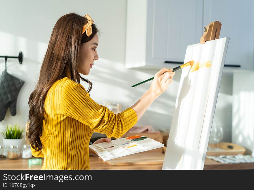 Asian young talented woman artist coloring on painting board in house. Attractive beautiful female draw art picture, creating artwork with watercolor paint and brush enjoy creativity activity at home