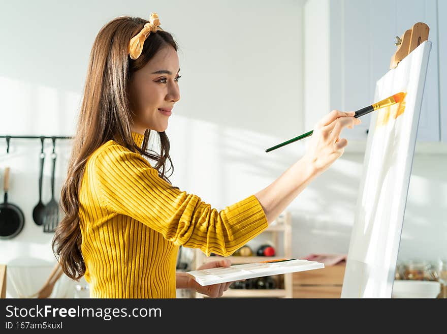 Asian young talented woman artist coloring on painting board in house. Attractive beautiful female draw art picture, creating artwork with watercolor paint and brush enjoy creativity activity at home