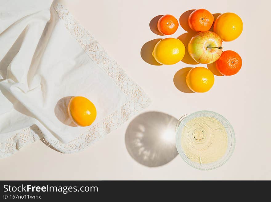 Creative composition made of glass with fruit juice, lemon, mandarin and apples on pastel beige sunlit background with white cloth and shadows. Summer and refreshment concept. Harvest theme
