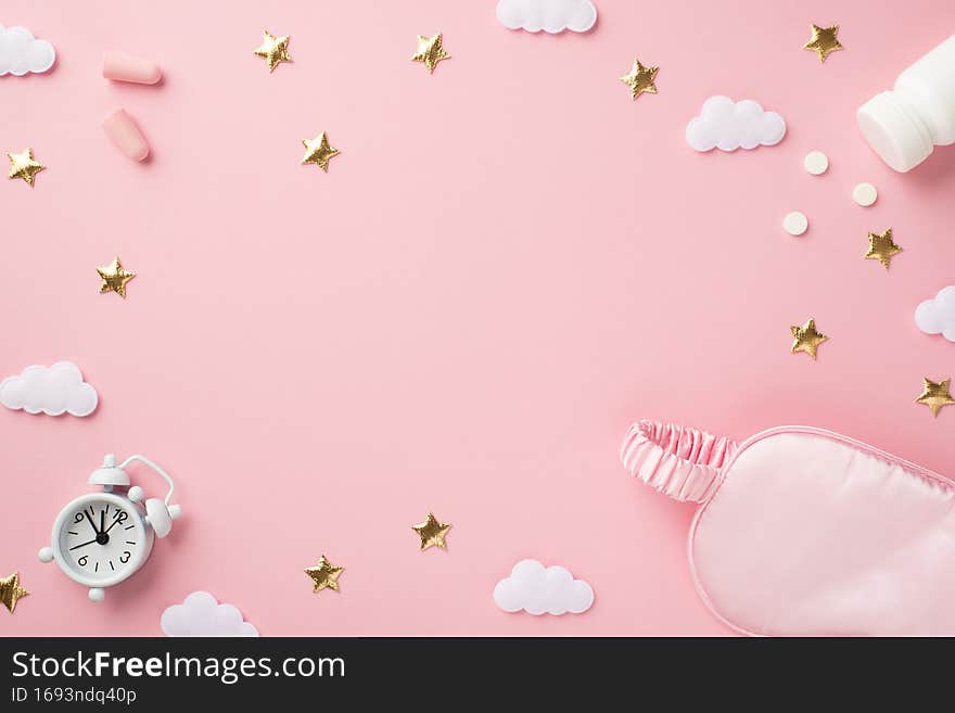 Top view photo of small white alarm clock pink silk sleeping mask earplugs bottle with pills golden stars and clouds on isolated