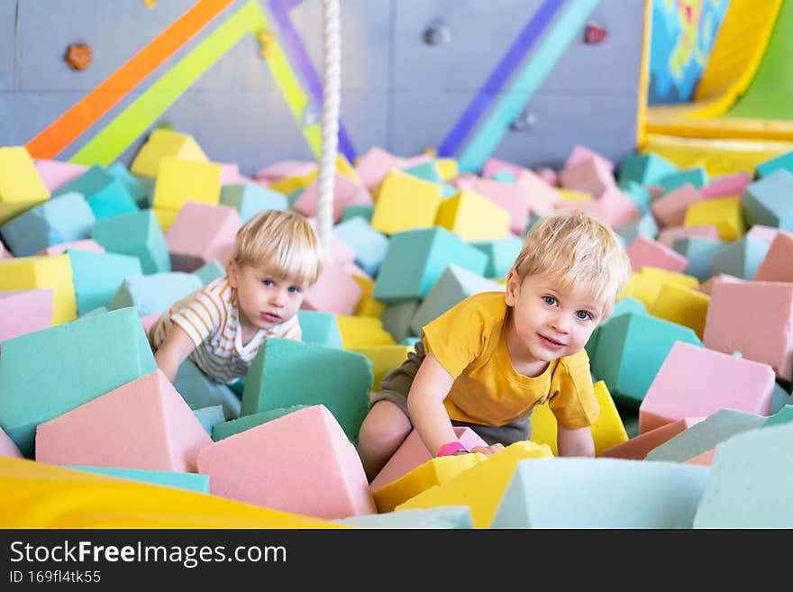 two cute little boys twins plays with soft cubes in the dry pool in play center.