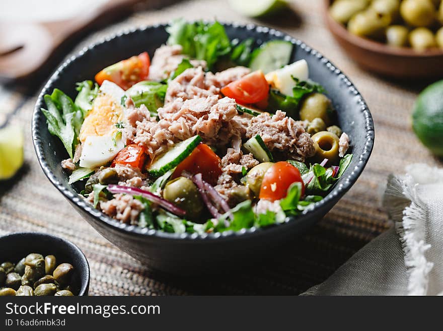 Canned tuna salad with fresh vegetables, capers and olives in a black bowl. Healthy lunch or dinner