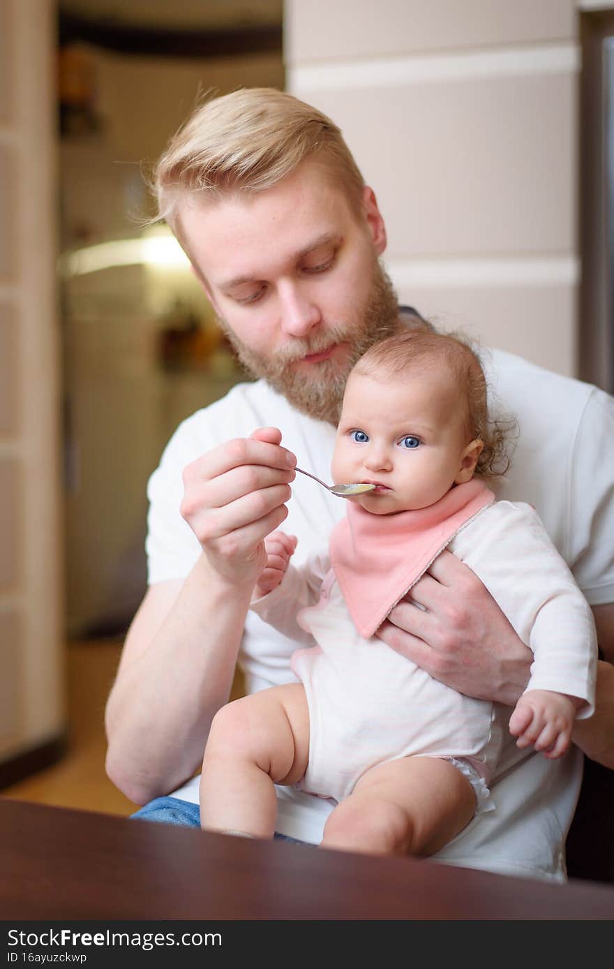 Father feeding his baby fruit puree in the kitchen