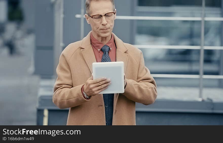 Middle aged businessman in coat using digital tablet on urban street,stock image