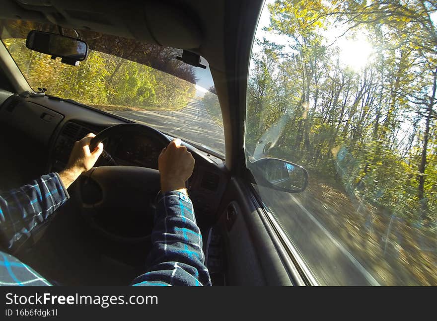 View from the interior of the car on a country road. In the foreground the driver's hands on the steering wheel. Travel concept