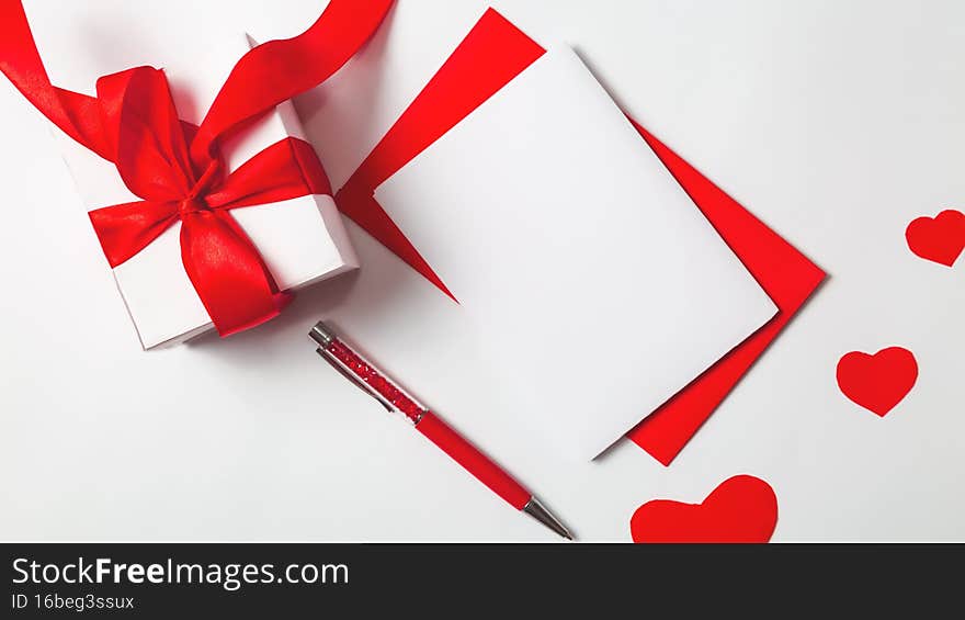 Gift box, envelope with blank note mockup and red hearts on a white background. Valentines day and romantic concept. Flat lay.