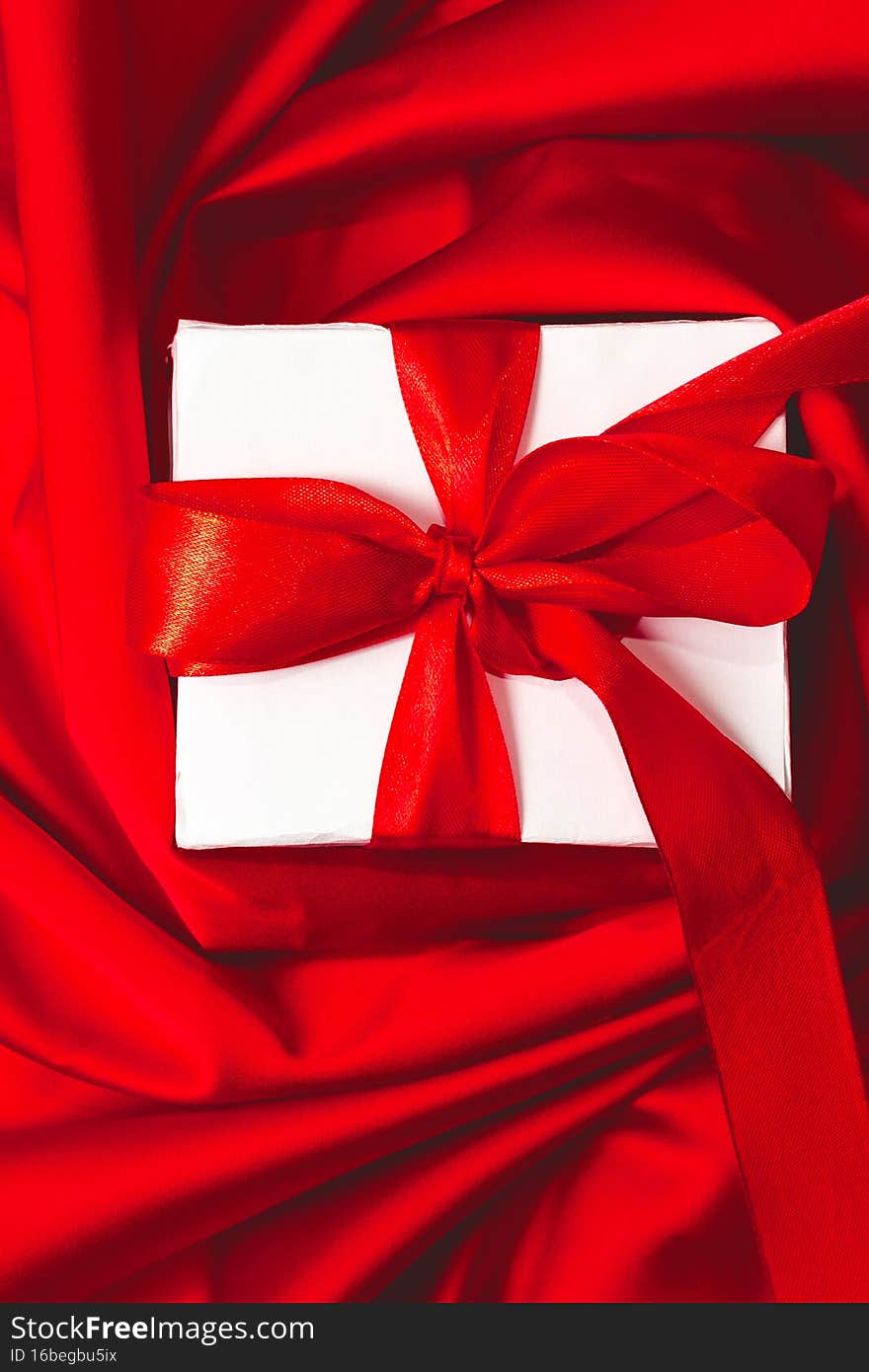 Valentine gift box with red ribbon bow on red silk texture satin fabric background. Banner design for St Valentines Day. Love and