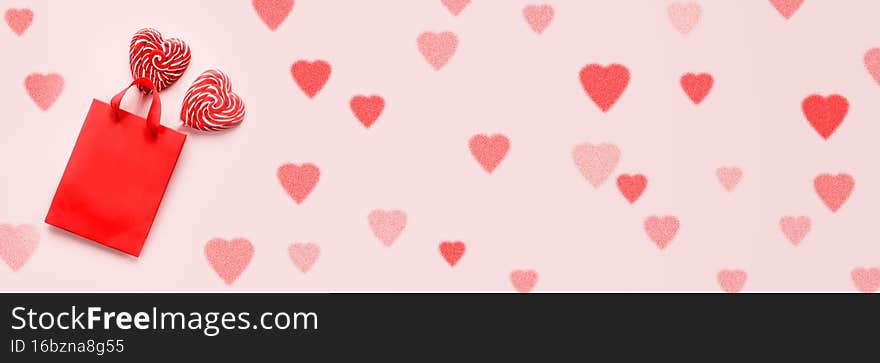 Red shopping bag with two heart shaped lollipops on pink Valentines day background banner size