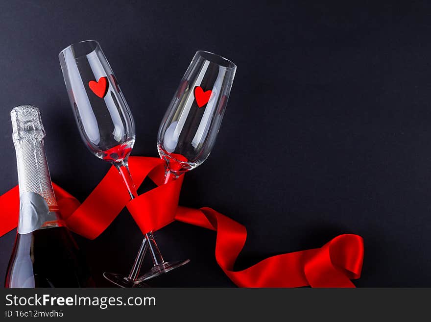 Heart shapes in empty flutes wrapped with red ribbon by champagne bottle. celebration glasses by copy space on black background.