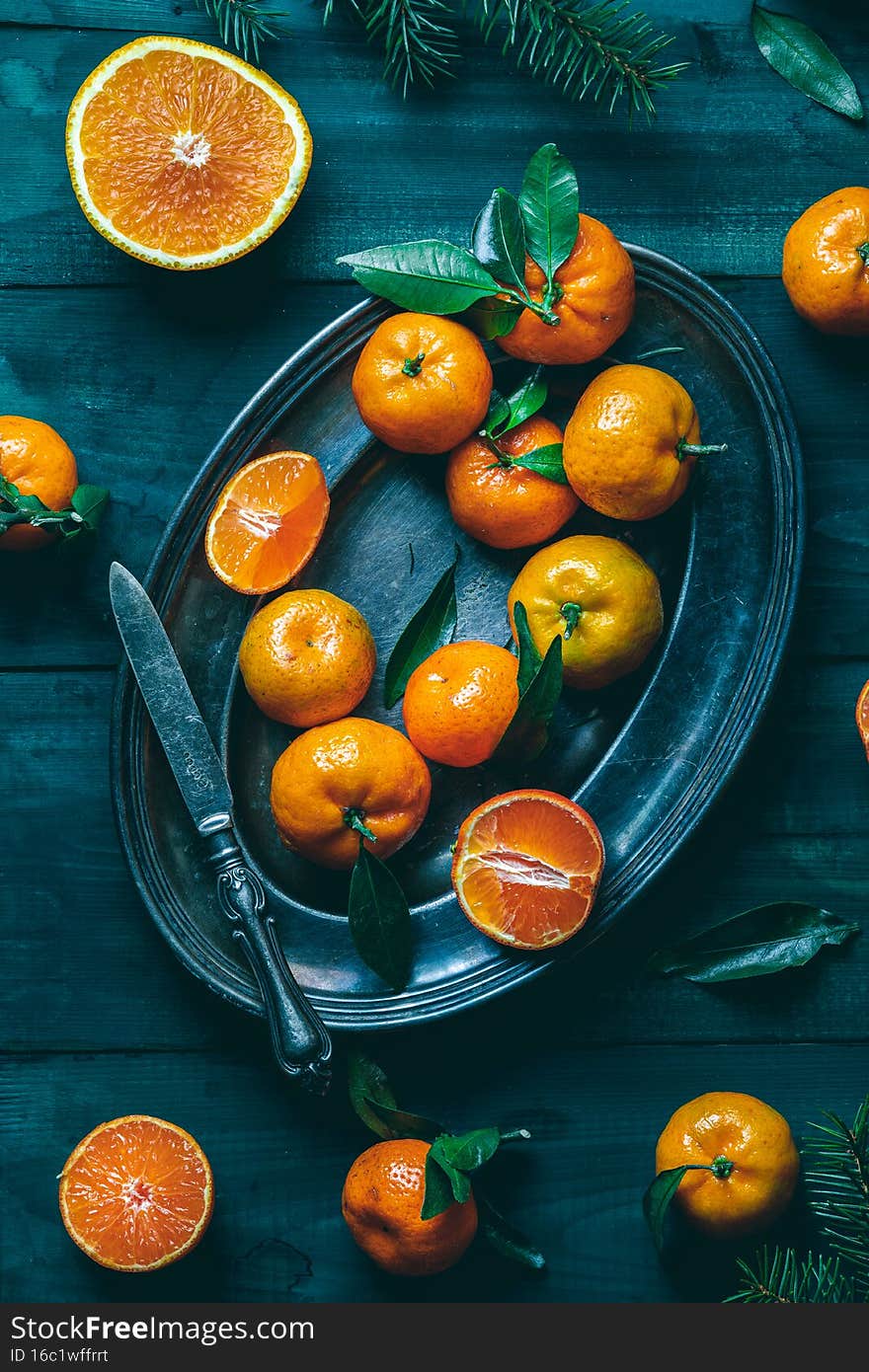 Tangerines with green leaves on a green wooden table in a rustic style surrounded by spruce branches. High quality photo