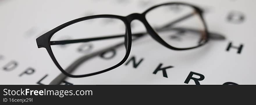 Beautiful glasses for sight lie on the alphabet. Modern black rimmed glasses on an eye test chart. Beautiful glasses for sight lie on the alphabet. Modern black rimmed glasses on an eye test chart