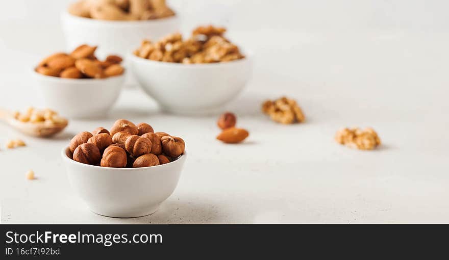 Hazelnuts and other nuts in white bowls on a white background. Banner