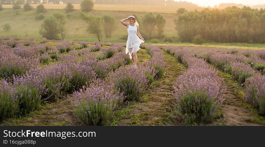 Beautiful young woman in wicker hat and white dress in a lavender field with