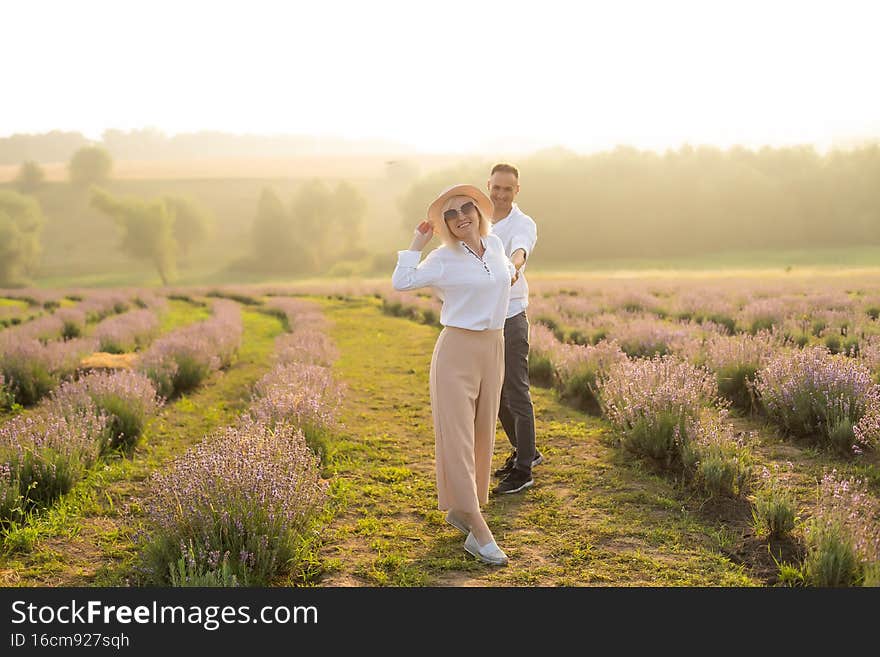 Smiling young couple embracing at the lavender field, holding hands, walking.