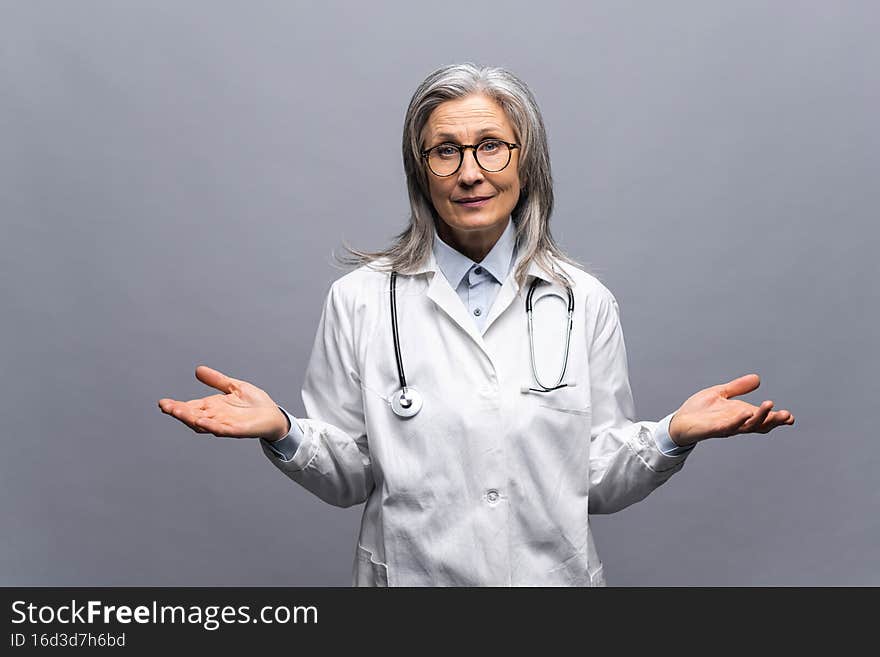 I dont know. Confused senior woman doctor throwing up her hands, puzzled, uncertain, cant find answer to question. Indoor studio shot isolated on gray background