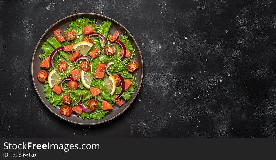 Salad with salmon and fresh vegetables on a black stone background. Top view, flat lay, copy space. Banner.
