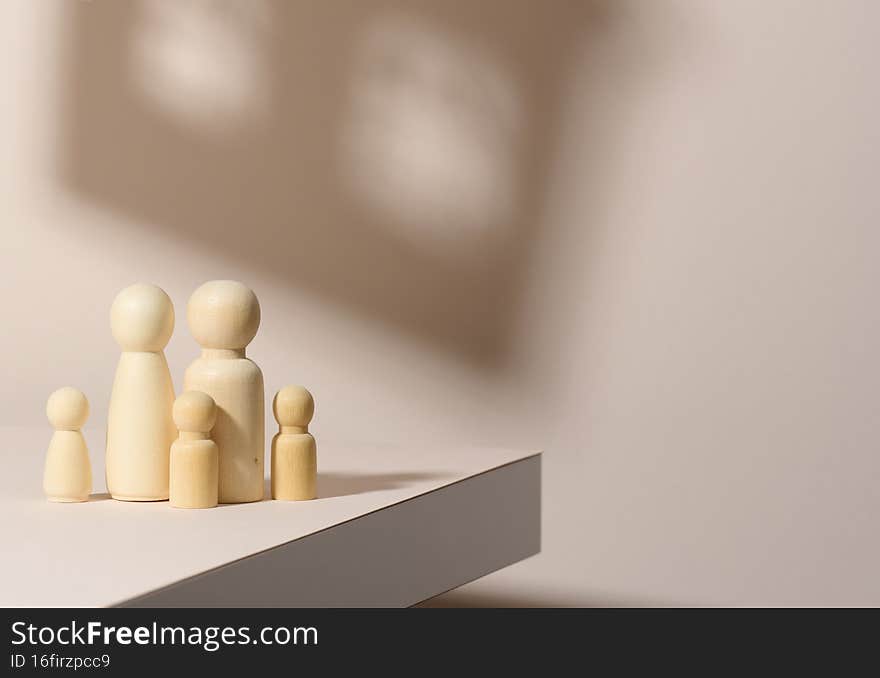 Wooden figurines of a family on a background of shadow in the form of a house. Beige background. Home dreams, mortgage.