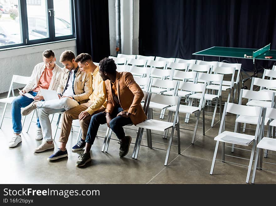 four young multicultural businessmen discussing startup project while sitting in conference hall,stock image