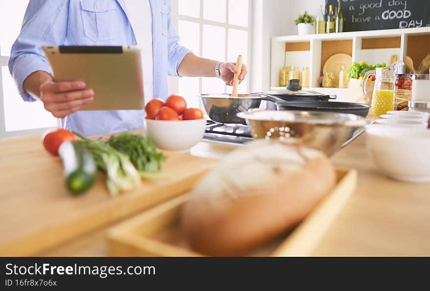 Man following recipe on digital tablet and cooking tasty and healthy food in kitchen at home