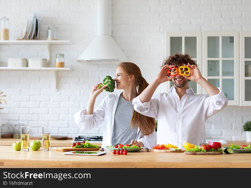 Smiling happy couple on the kitchen cooking having fun man covering eyes with paprika woman holding broccoli