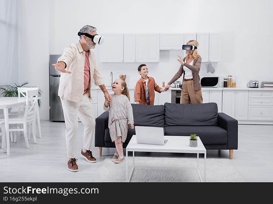 couple in vr headsets holding hands with grandchildren while gaming in kitchen,stock image