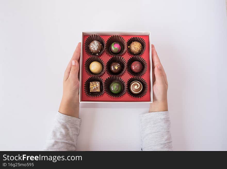 Children`s hands with delicious chocolate candies in a box on a white background