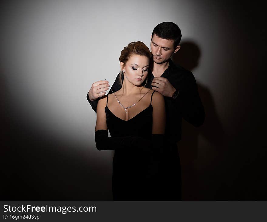 To give diamonds. Men's hands fasten a pendant with jewelry around the neck of their beloved. Beautiful young blonde in a black dress with a neckline. To give diamonds. Men's hands fasten a pendant with jewelry around the neck of their beloved. Beautiful young blonde in a black dress with a neckline.