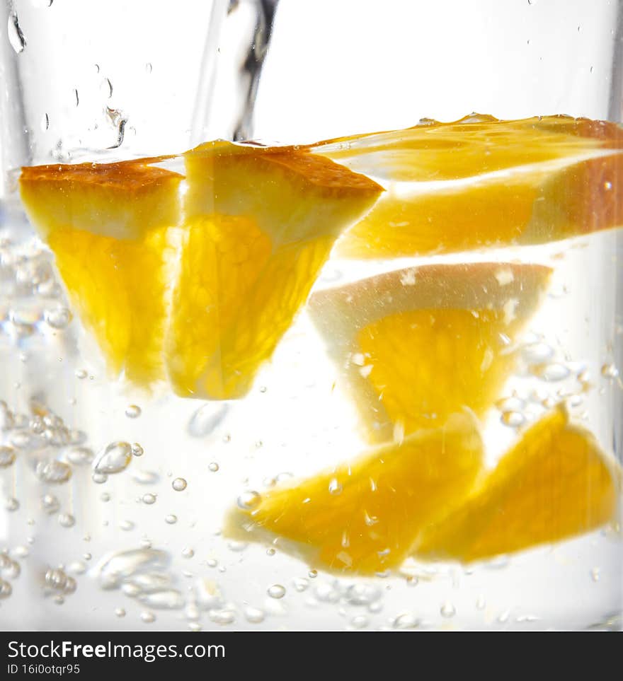 Closeup of transperent glass of water and bubbles in it as a backgruond Fresh tatsy pieces of oranges and pouring water.Fresh summer drink