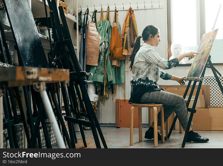 A talented young artist paints a picture with oil paints in a soiled shirt in a creative workshop, where the canvas is on an easel. A talented young artist paints a picture with oil paints in a soiled shirt in a creative workshop, where the canvas is on an easel.