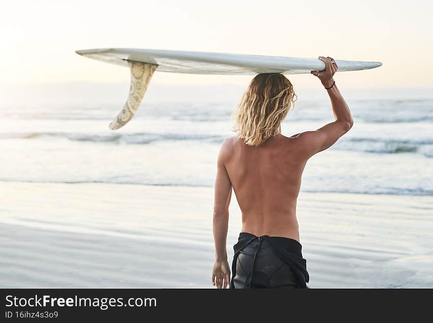 He& x27;s riding the waves today. Rearview shot of a young surfer carrying his surfboard over his head at the beach.