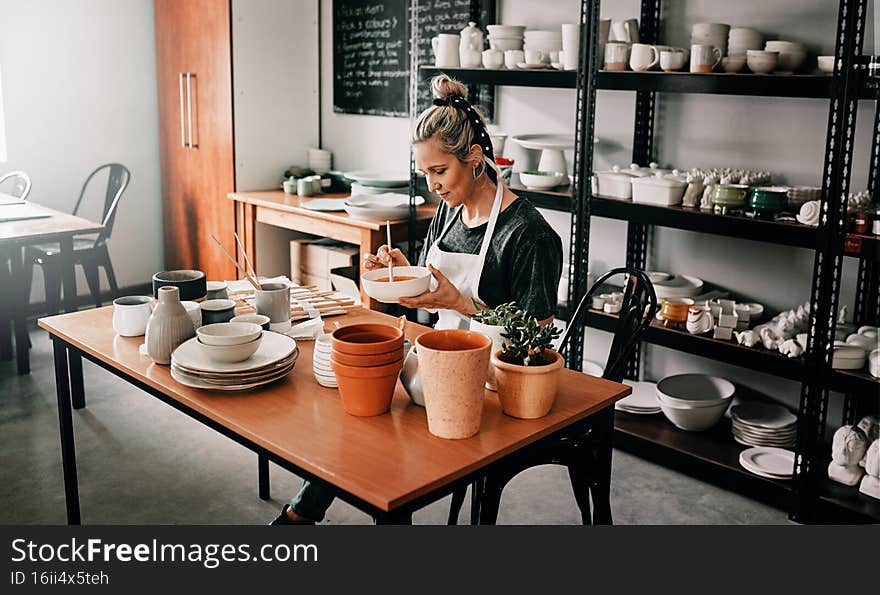 Cropped shot of an attractive mature woman sitting alone and painting a pottery bowl in her studio. Cropped shot of an attractive mature woman sitting alone and painting a pottery bowl in her studio
