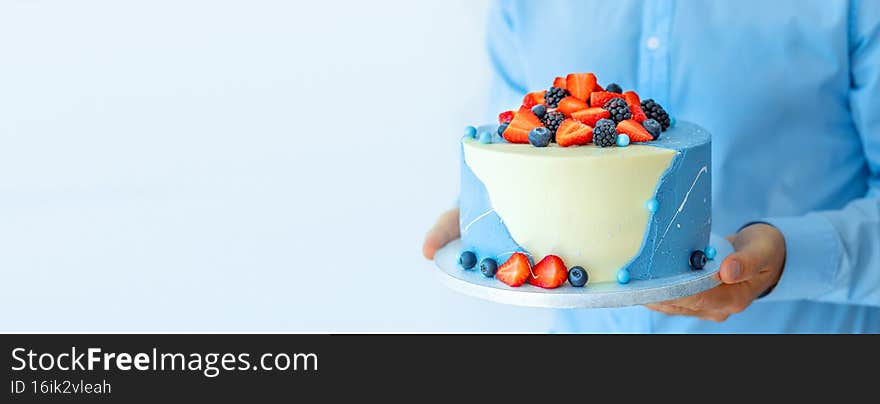 A man pastry shef holding a beautiful big cake with berries in his hands. Male chef cook confectioner or baker. Mock up