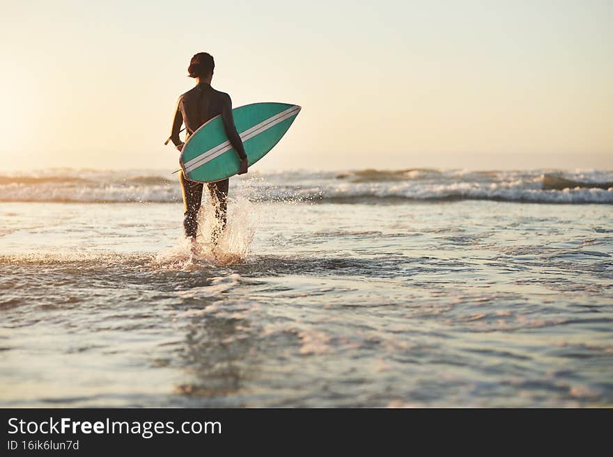 Rearview shot of a young woman going surfing at the beach. Rearview shot of a young woman going surfing at the beach