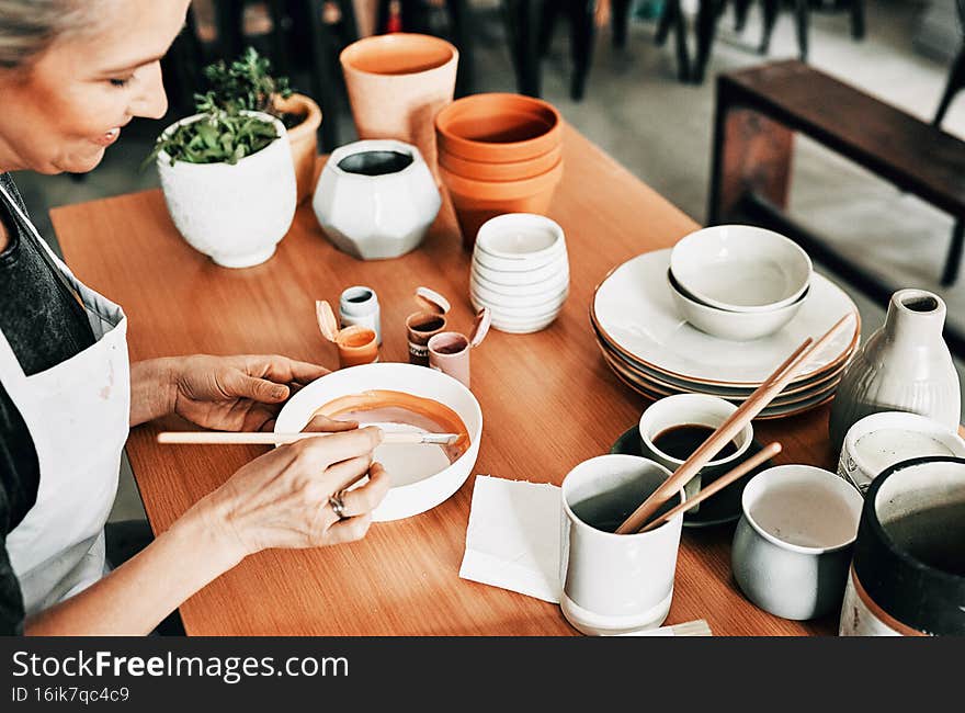 Cropped shot of an attractive mature woman sitting alone and painting a pottery bowl in her studio. Cropped shot of an attractive mature woman sitting alone and painting a pottery bowl in her studio