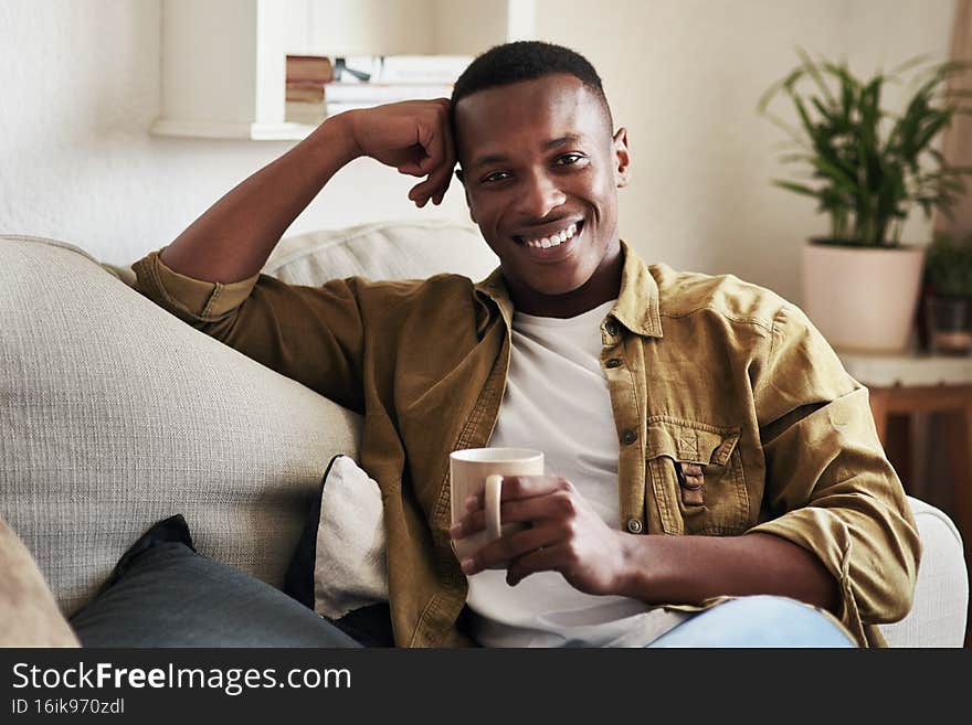 Cropped portrait of a handsome young man smiling while having coffee on his couch at home. Cropped portrait of a handsome young man smiling while having coffee on his couch at home