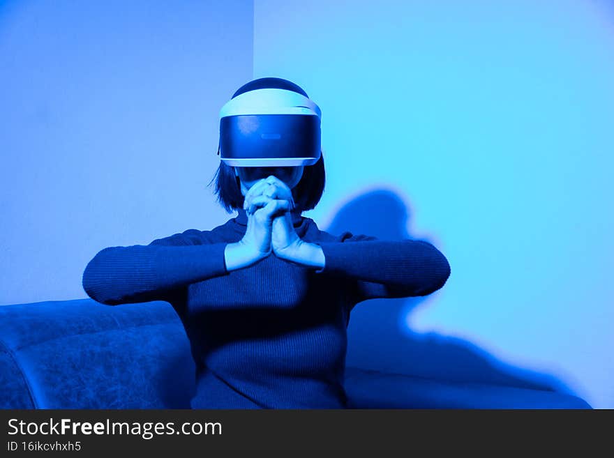 Beautiful woman using vr headset keep hands together, shaking, greeting at home in blue light. Virtual business concept
