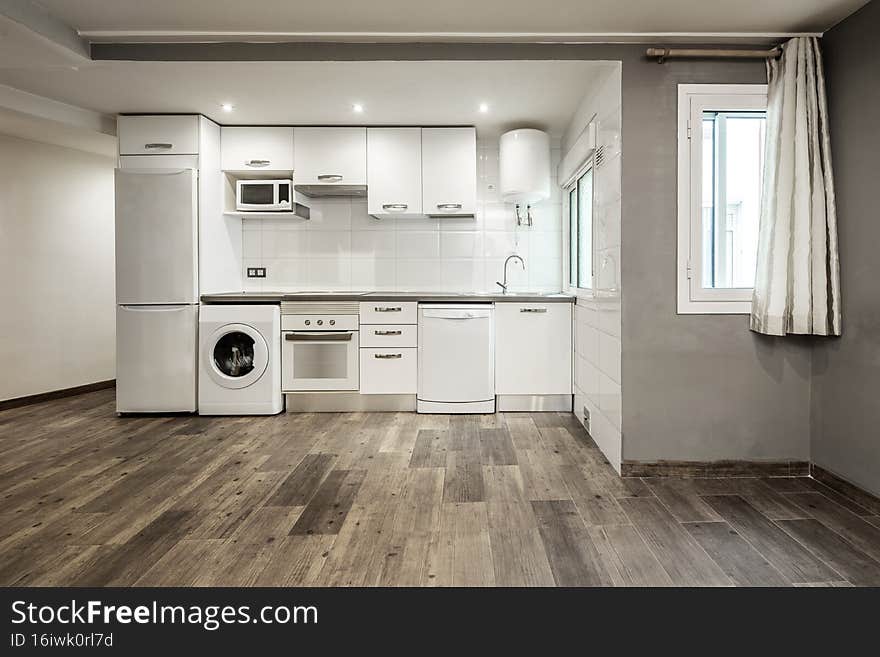 Kitchen with white furniture and matching appliances on one side of a vacation rental studio with wooden floors