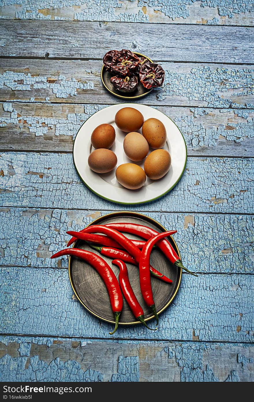 Plate with raw eggs, red hot chili peppers and dry peppers on blue wooden table