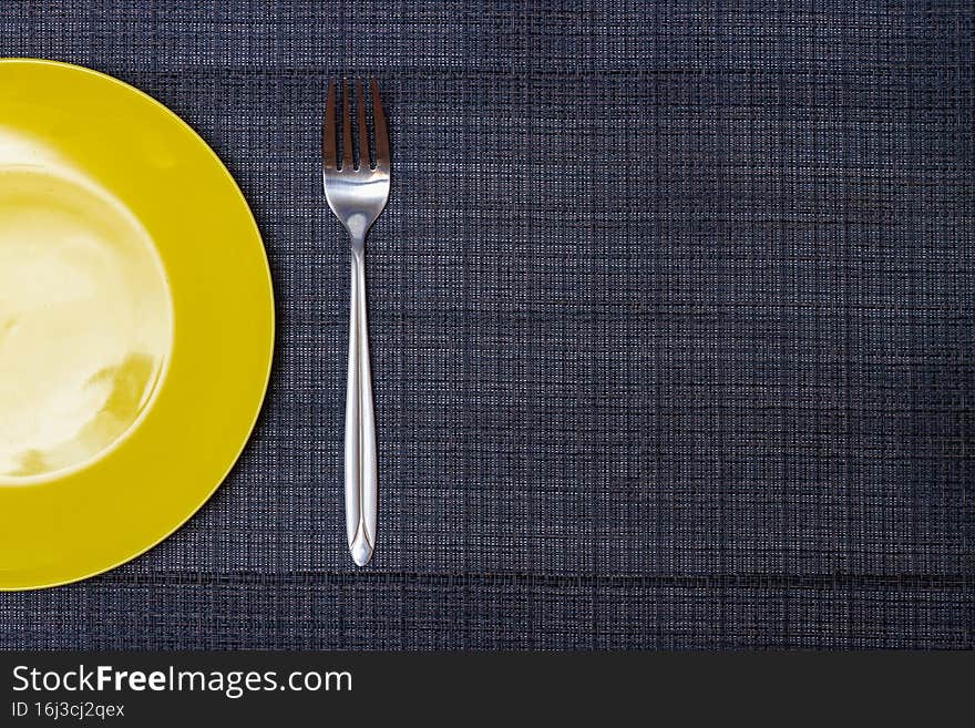 A yellow plate with a fork on a gray napkin. Copy Space.